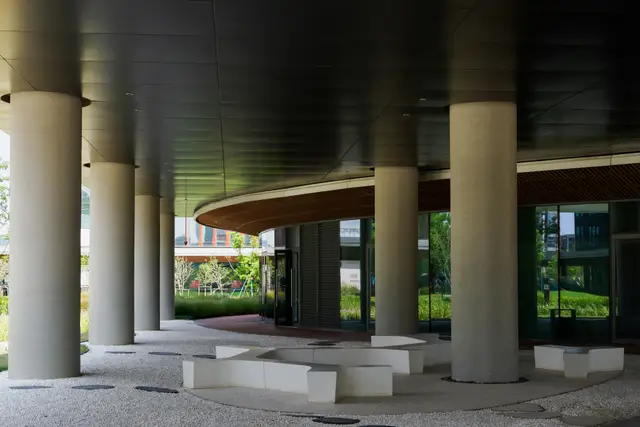 A covered building entrance, with concrete columns and low benches beneath a curved soffit.