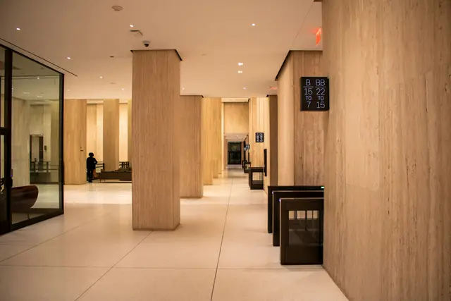 A travertine-clad office lobby, its columns and glazed partitions receding toward a security gate.