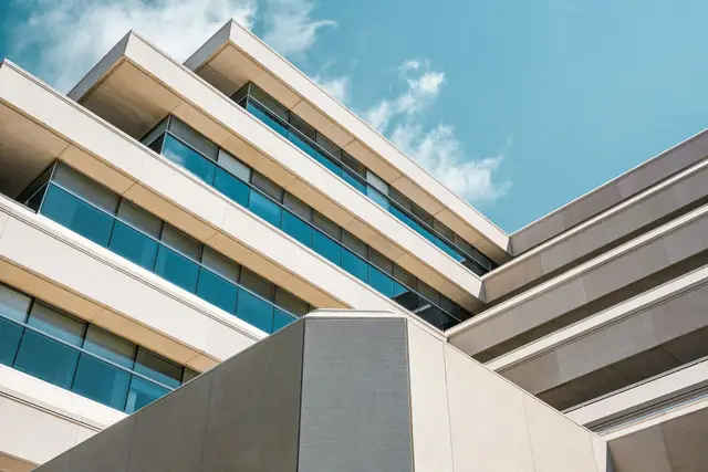A beige concrete office building seen from below, its floors stepping back against a clouded sky.