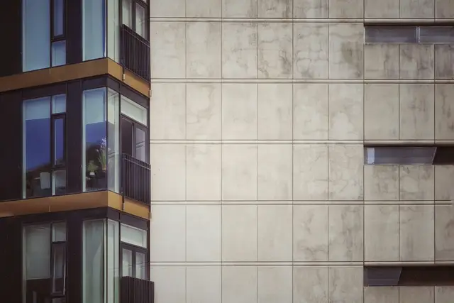 A building façade of plain concrete panels meeting a run of glazed balconies, photographed square on.