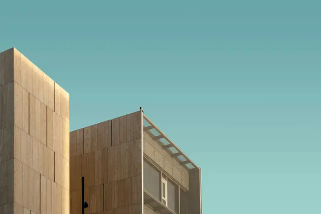 A timber-clad office tower meeting a plainer neighboring block, photographed from below against a clear sky.