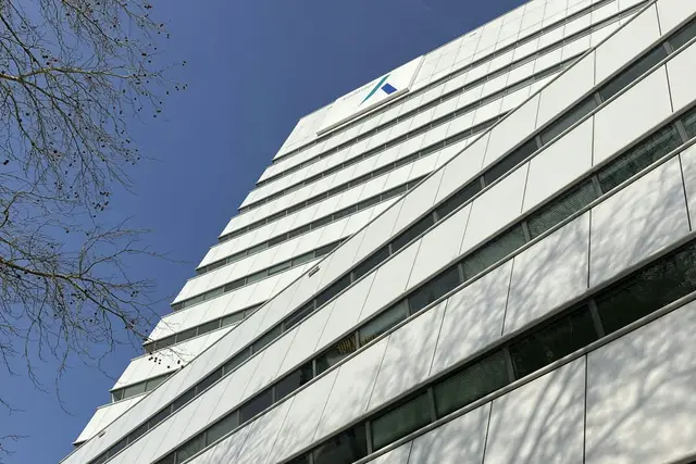 A white office building photographed from below, its angled façade panels stepping up against a clear sky.